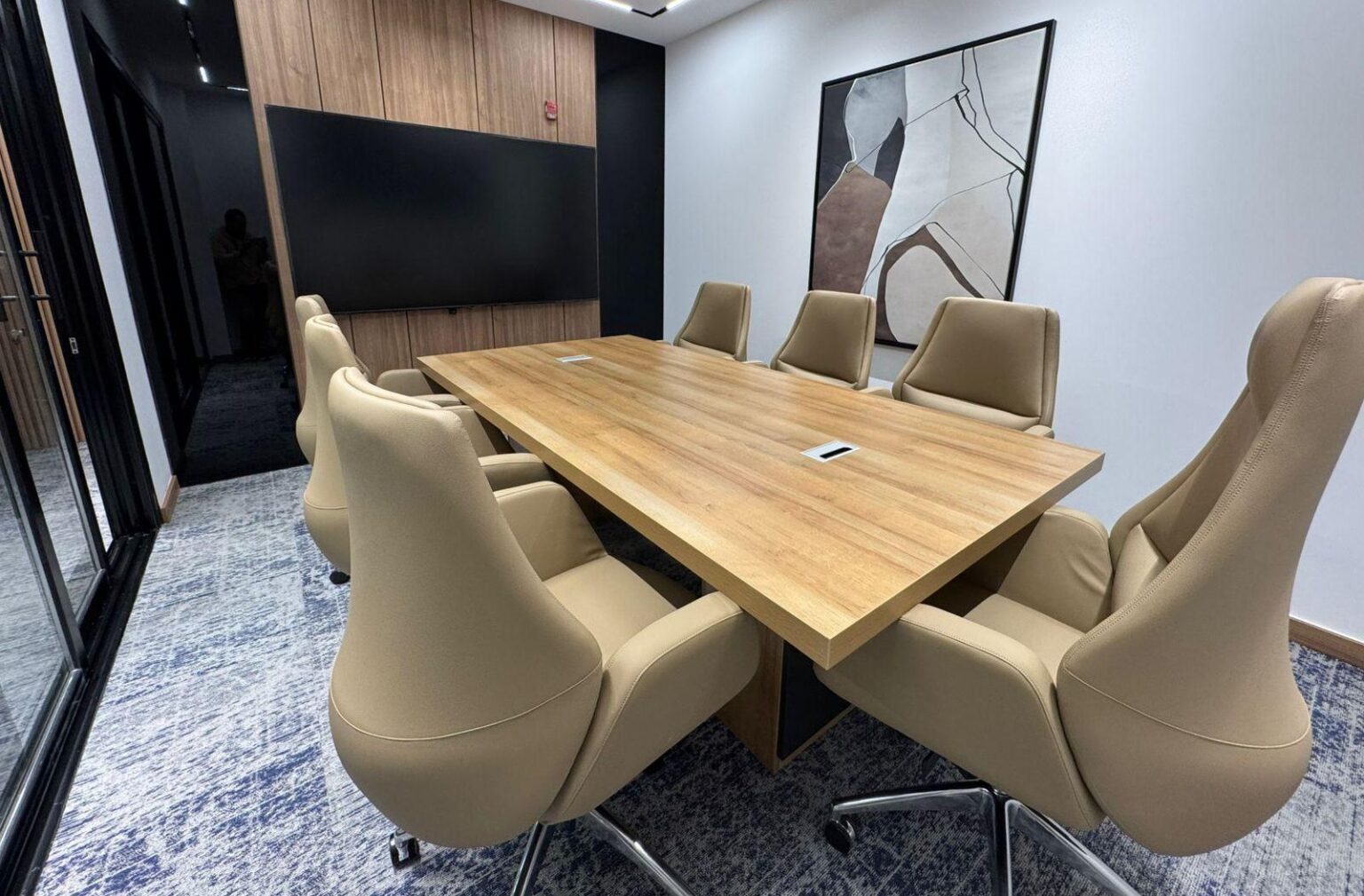 A high-end conference room with beige leather chairs, a wooden table, and abstract wall art.